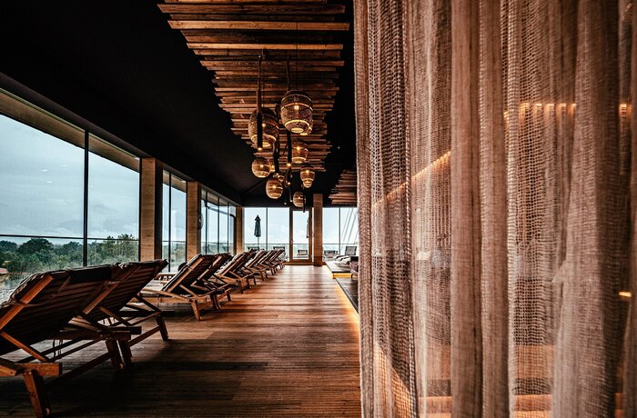 Spa-Bereich mit Liegen, Holzboden, großen Fenstern und dekorativen Lampen unter einer Holzdecke