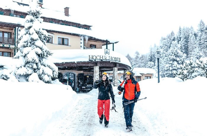 Zwei Skifahrer vor schneebedecktem Hotel HochSchober mit Skiern auf der Schulter