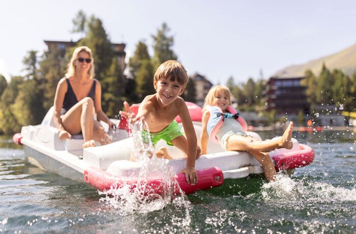Familie auf Tretboot, Junge spritzt Wasser, Mädchen und Frau lächeln