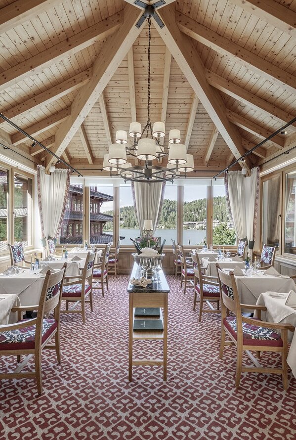 Restaurant mit Holzbalkendecke, Kronleuchter, gedeckten Tischen und Blick auf einen See