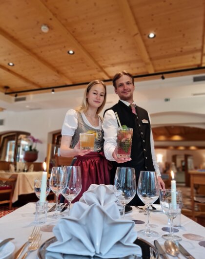 Kellnerpaar in Tracht präsentiert Cocktails am gedeckten Tisch