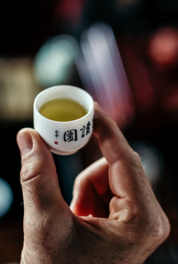 A person is holding a small teacup filled with light-colored tea.