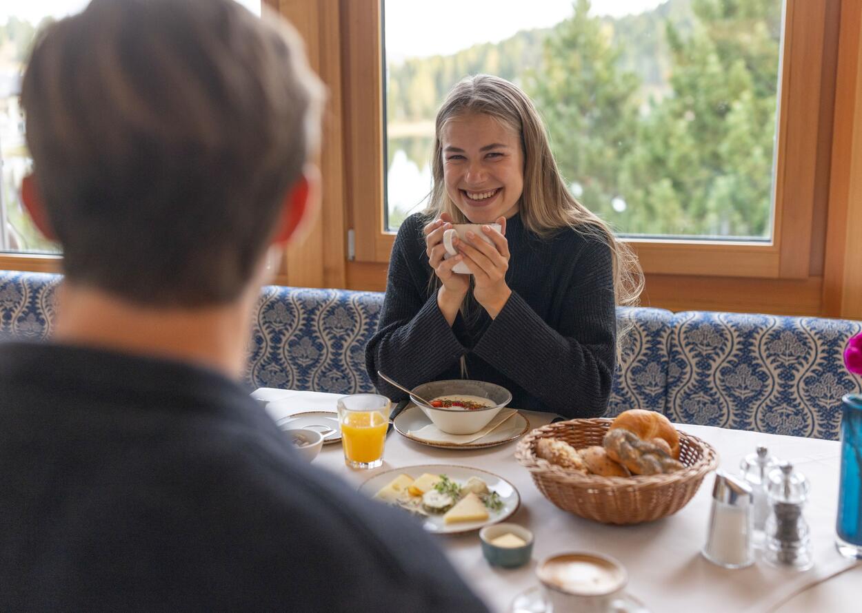 Frau beim Frühstück mit Kaffee und Gebäck am Fensterplatz.
