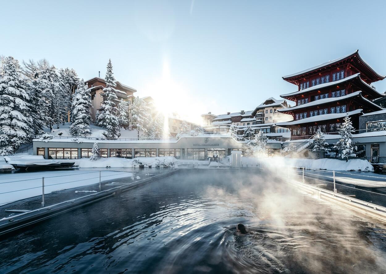 Winterliches Seebad mit Hotelanlage unter strahlender Sonne, Dampf steigt über dem Wasser auf