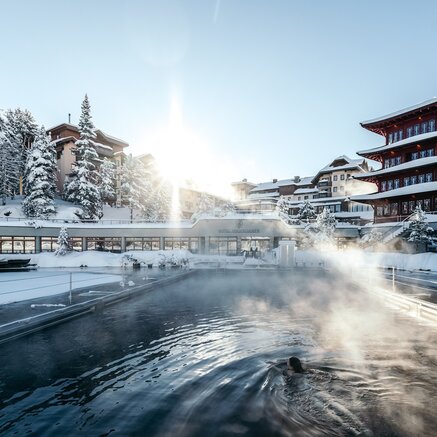 Winterliches Seebad mit Hotelanlage unter strahlender Sonne, Dampf steigt über dem Wasser auf