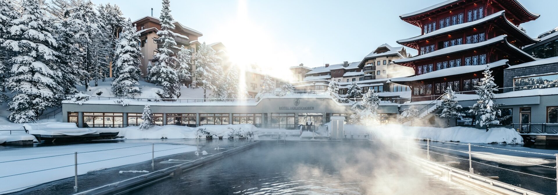 Winterliches Seebad mit Hotelanlage unter strahlender Sonne, Dampf steigt über dem Wasser auf