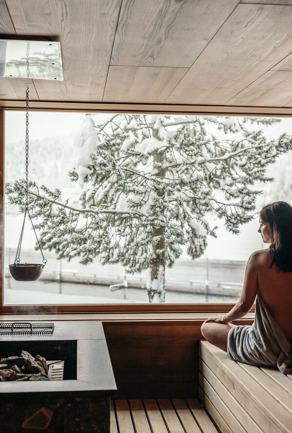 Woman in herbal sauna looks through window at snowy landscape
