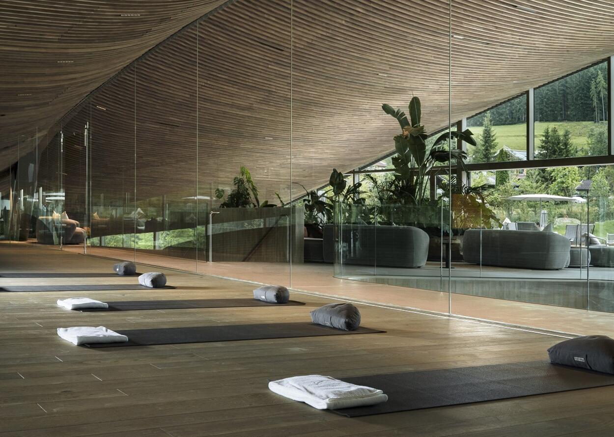 Heller Yogaraum mit Matten, Kissen und Pflanzen hinter Glaswänden