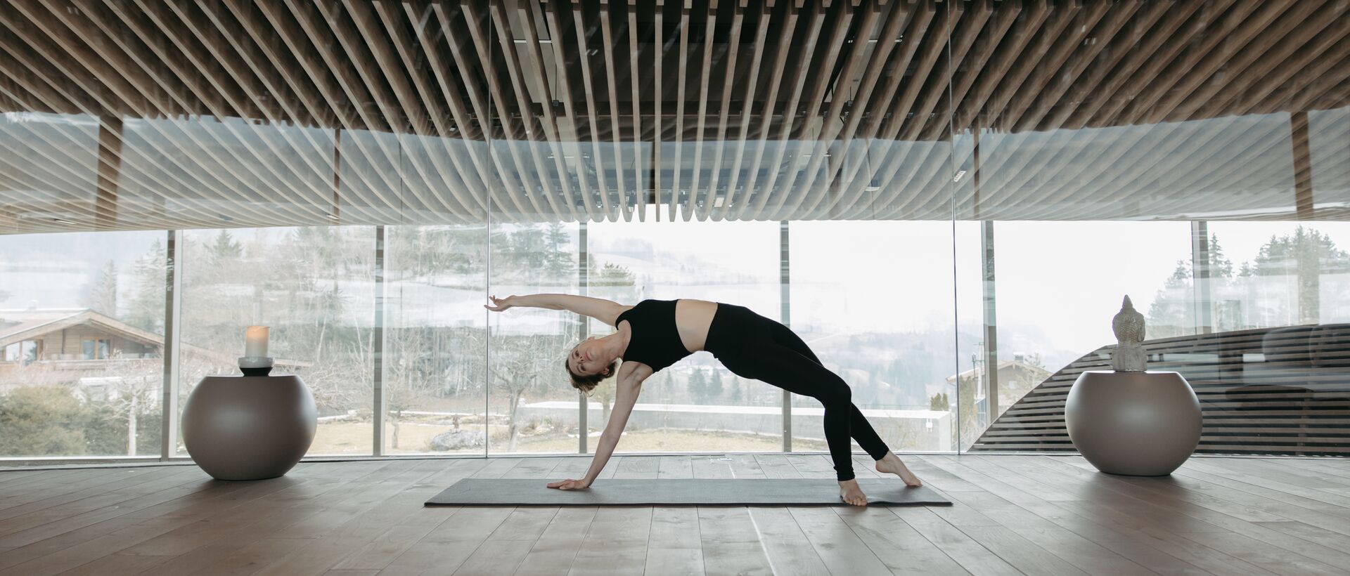 Frau macht Yoga in hellem Raum mit Holzdecke und Panoramafenster