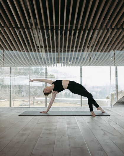 Woman doing yoga in bright room with wooden ceiling and panoramic window