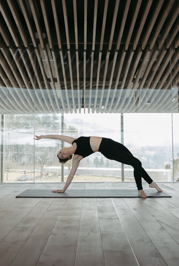Frau macht Yoga in hellem Raum mit Holzdecke und Panoramafenster
