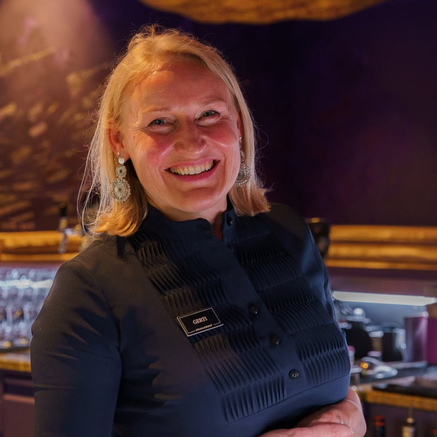 Lächelnde blonde Frau mit Namensschild Gerti vor dunklem Hintergrund