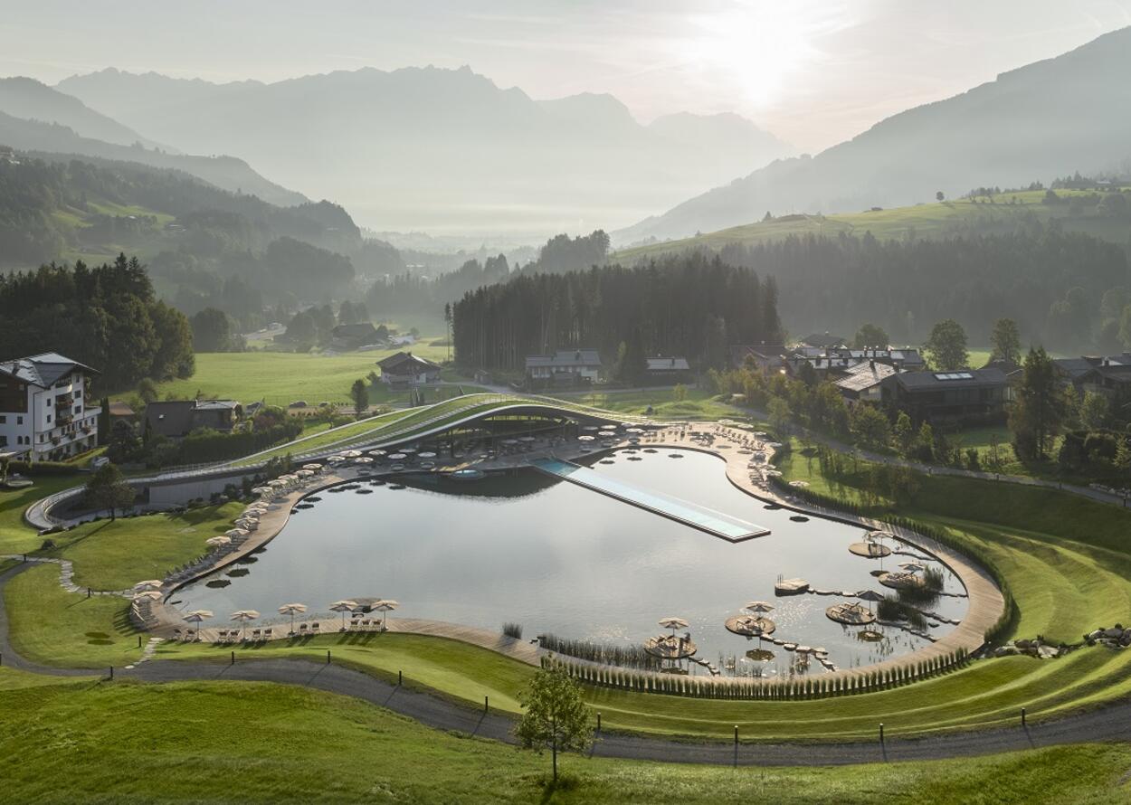 Panorama des Krallerhofs im Sommer mit See, Liegeflächen und Bergen im Hintergrund