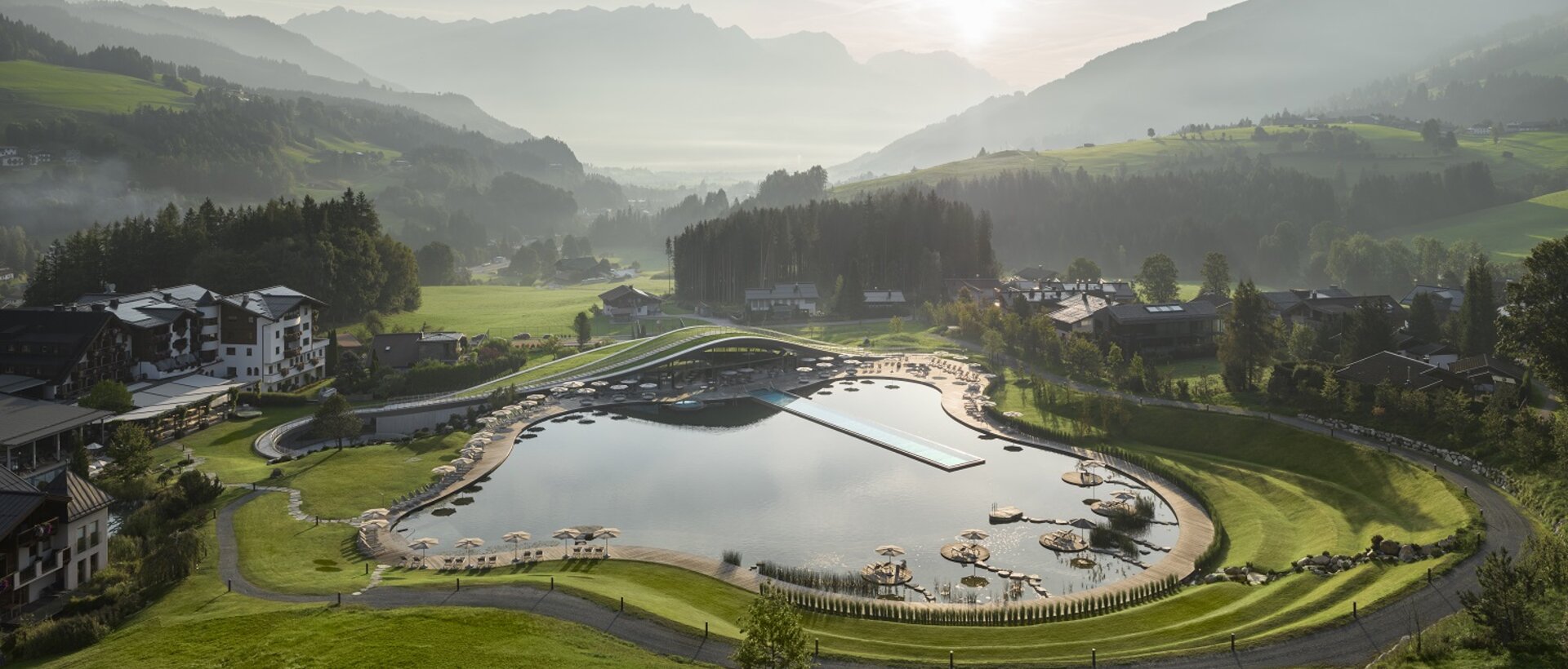 Panorama des Krallerhofs im Sommer mit See, Liegeflächen und Bergen im Hintergrund