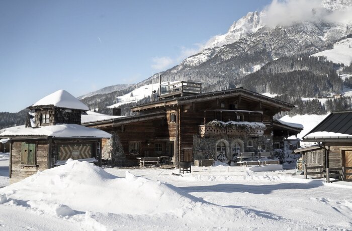 KrallerAlm im Winter mit Schneebergen vor dem Holzgebäude und schneebedeckten Bergen im Hintergrund