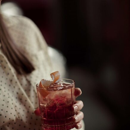 Woman holding cocktail glass with ice cubes and red liquid