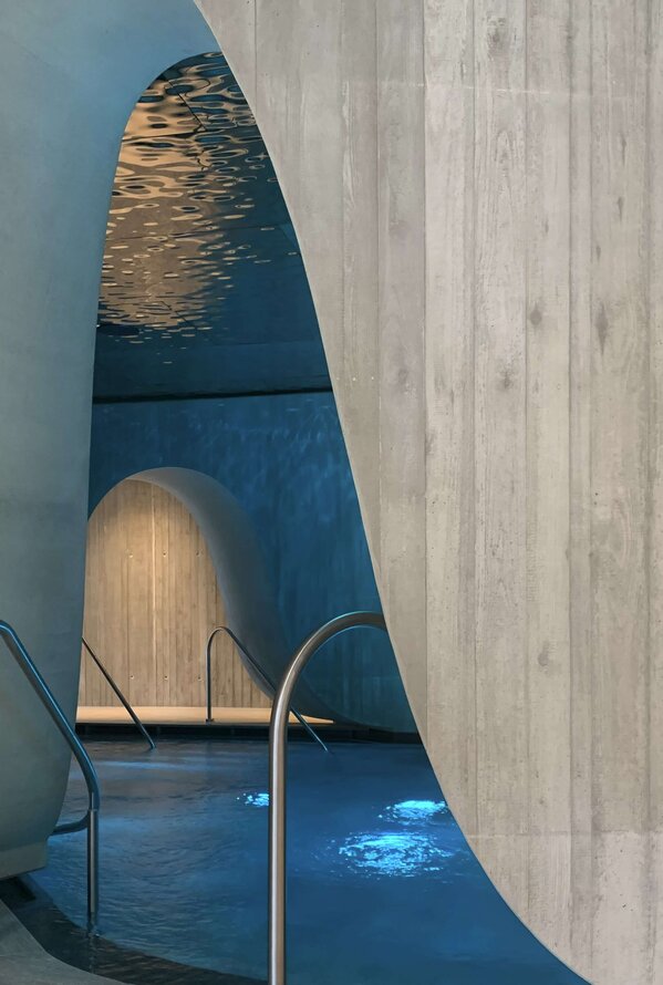 Schwimmbad mit geschwungenen Betonwänden und Wasserreflexionen an der Decke