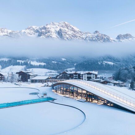 Winterlandschaft mit schneebedeckten Bergen, Häusern und Schwimmbadanlage