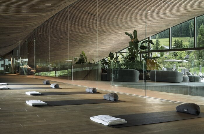 Heller Yogaraum mit Matten, Handtüchern und Pflanzen vor großen Glasfenstern