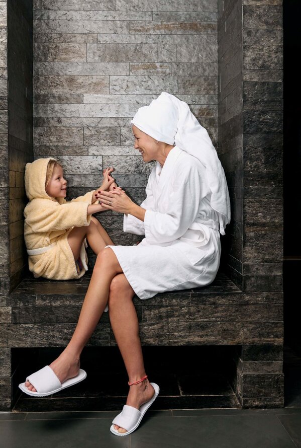Mutter und Kind im Bademantel sitzen in einer Steinsauna und spielen