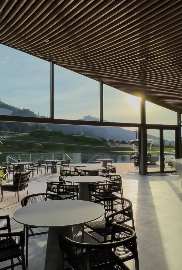 Moderner Lounge- und Barbereich mit Panoramafenstern und Blick auf die Berglandschaft bei Sonnenuntergang