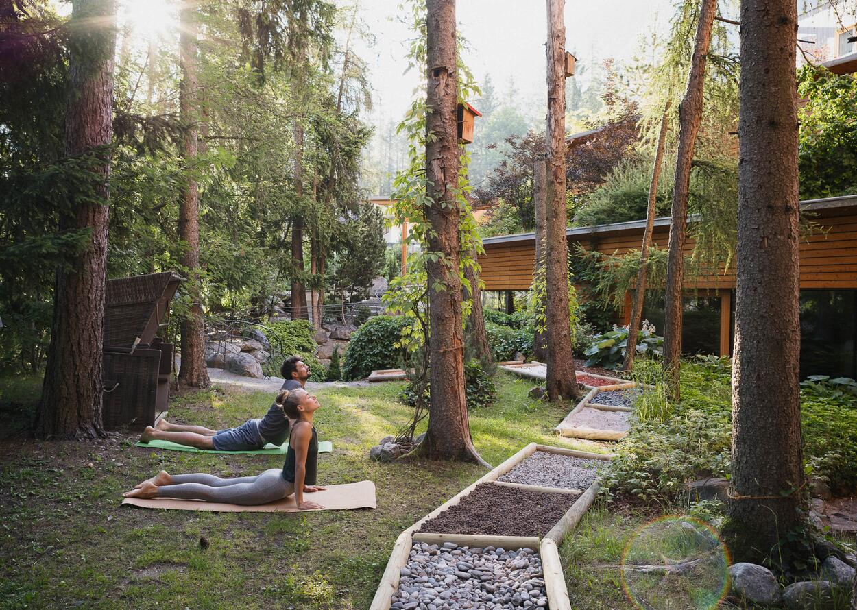 Zwei Menschen machen Yoga im Waldgarten zwischen Bäumen und Natur.