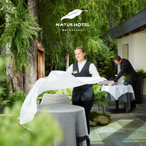 Kellner decken Tische im Außenbereich eines Hotels mit dem Logo Naturhotel Waldklause