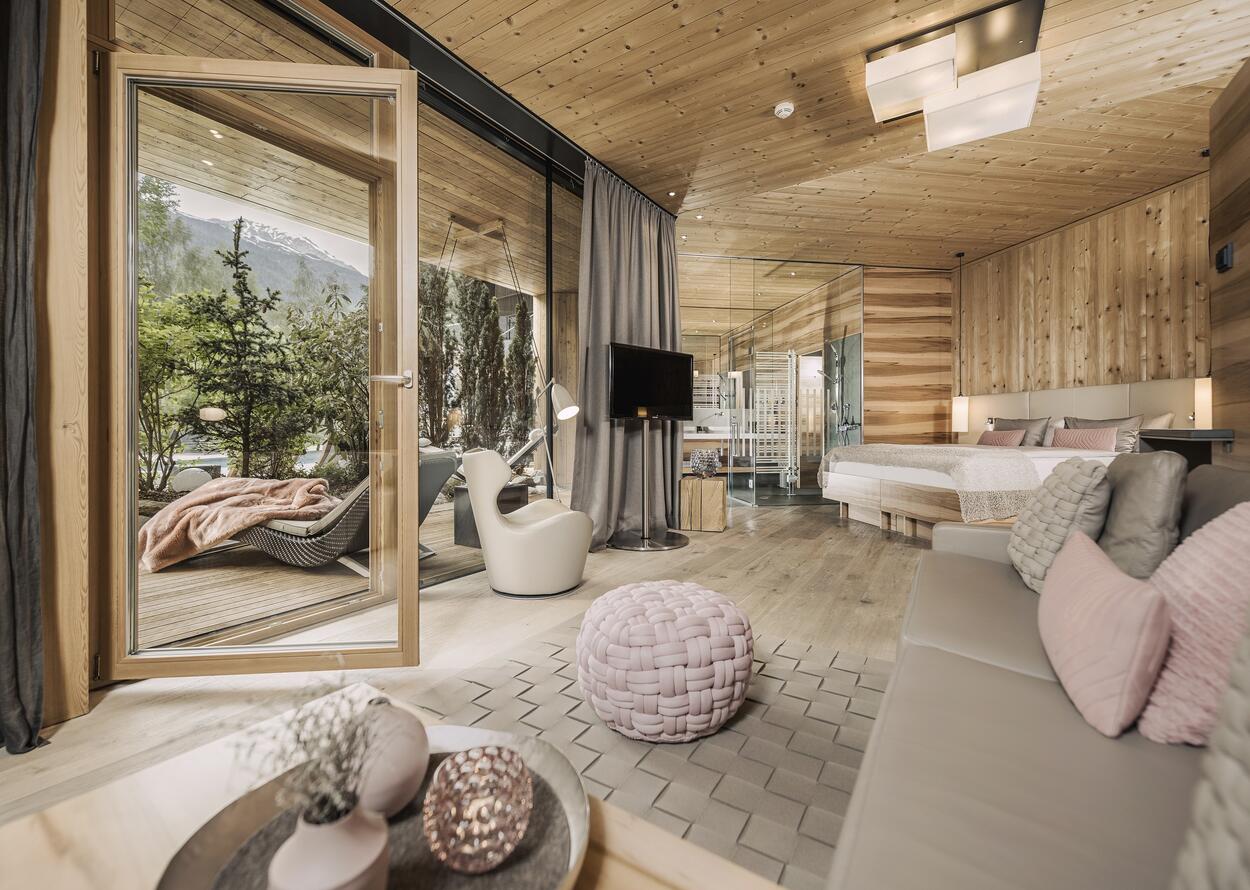 Modernes Hotelzimmer im Naturhotel Waldklause mit Holzinterieur, offenem Wohnbereich und Terrasse mit Bergblick
