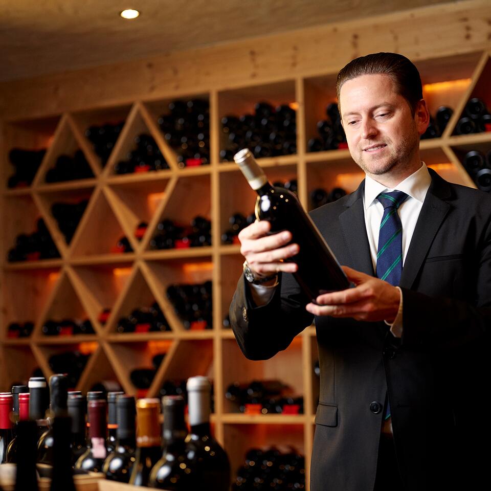 Ein Sommelier präsentiert eine Weinflasche in einem stilvollen Weinkeller mit großer Auswahl an edlen Weinen.