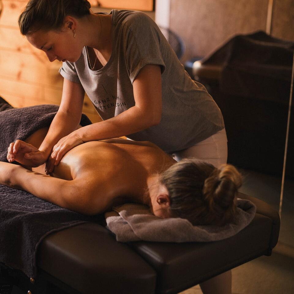 Frau massiert Rücken einer liegenden Person auf einer Massageliege