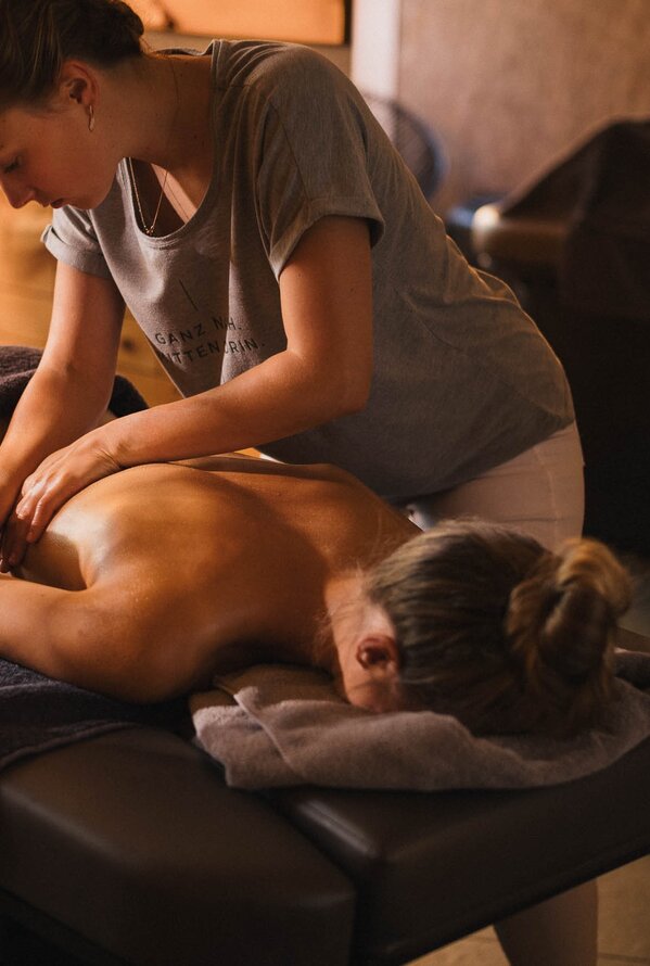 Frau massiert Rücken einer liegenden Person auf einer Massageliege