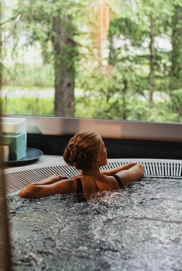 Eine Frau entspannt in einem Whirlpool mit Blick auf den Wald.