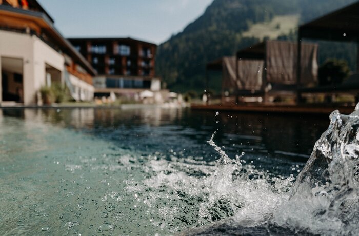 Wasser spritzt vor Hotelkulisse mit Bergen im Hintergrund