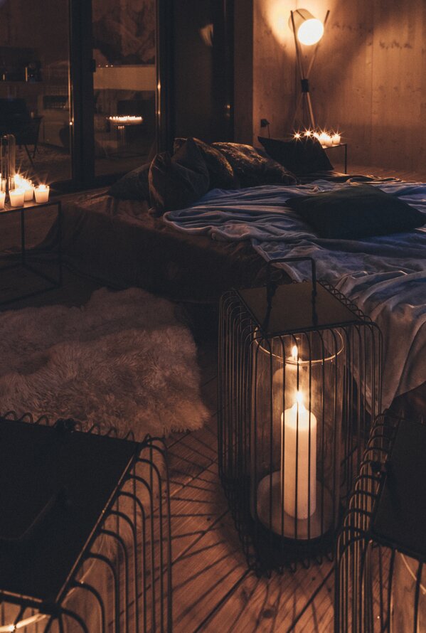 A cozy terrace at night with candlelight, soft cushions, and a view over a lit mountain village. The warm lighting creates a relaxing and romantic atmosphere.