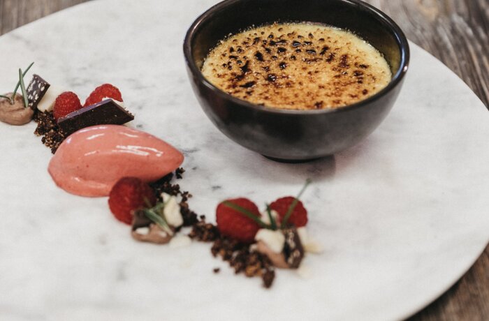 Crème brûlée with raspberry sorbet, chocolate pieces and fresh raspberries on a white plate