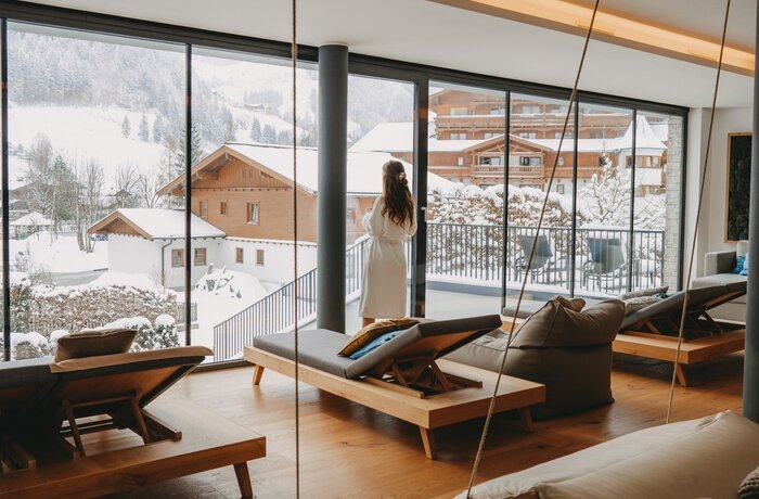 Woman in bathrobe looks out of relaxation room window at snowy winter landscape