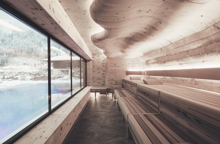 Bright sauna with wooden loungers, curved ceiling and large window with outside view