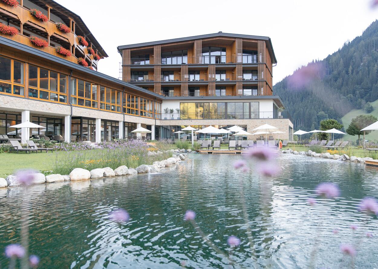 Hotel Nesslerhof with pond and lawn in summer against a mountain backdrop