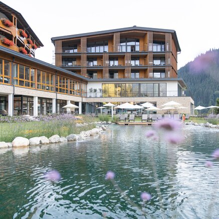 Hotel Nesslerhof mit Teich und Liegewiese im Sommer vor Bergkulisse