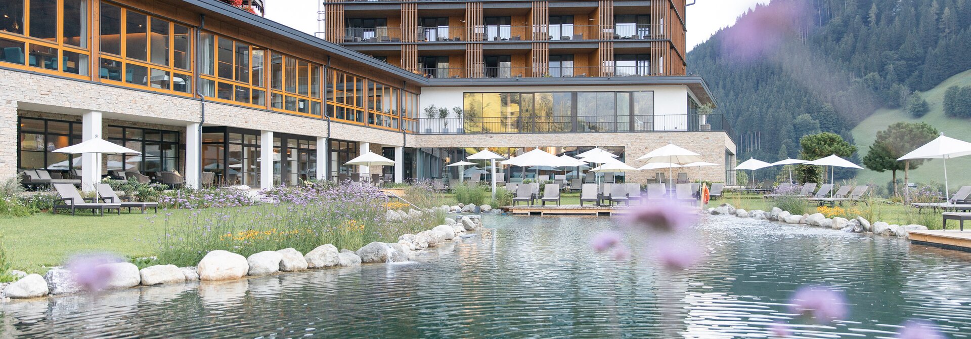 Hotel Nesslerhof mit Teich und Liegewiese im Sommer vor Bergkulisse