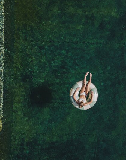 Drone view of a woman floating on an inflatable ring in a natural pool with clear water