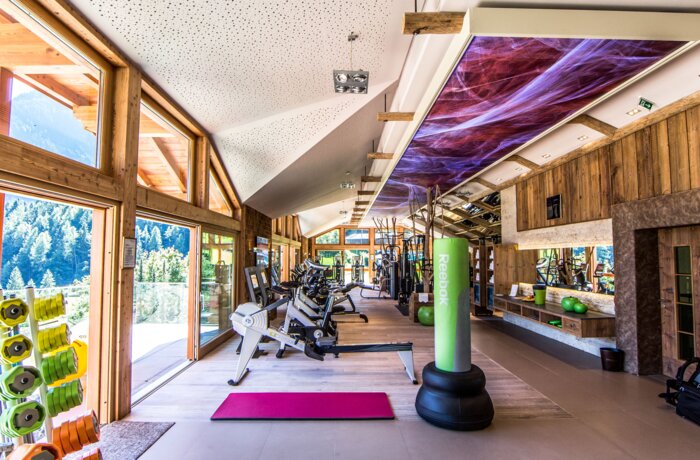 Helles Fitnessstudio mit Holzverkleidung, großen Fenstern und verschiedenen Trainingsgeräten