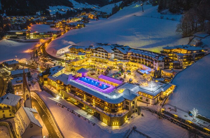 Beleuchtetes Hotel mit Pool im Schnee, abendliche Winterlandschaft mit Lichtern