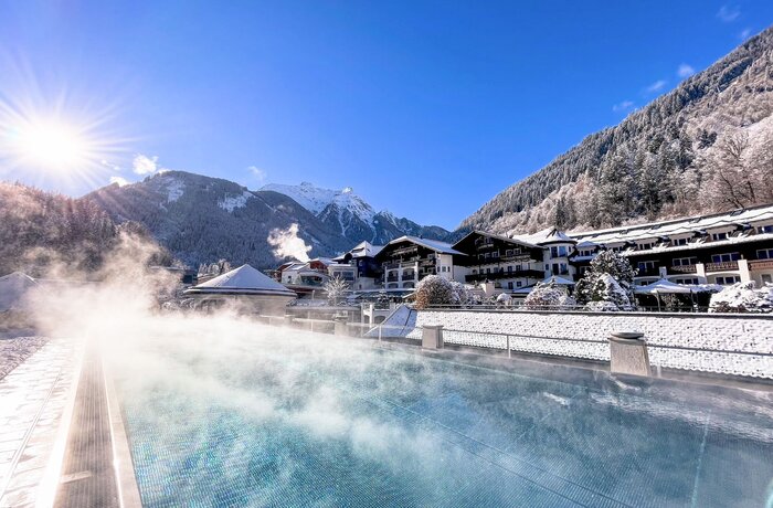 Winter pool with steam, in the background snow-covered mountains and houses on the Grünberg