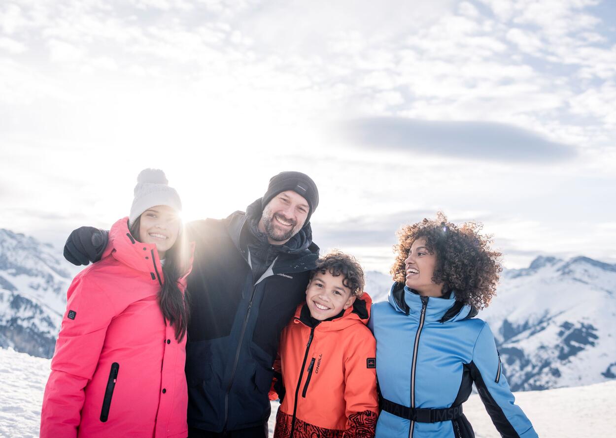 Fröhliche Familie genießt gemeinsam einen sonnigen Wintertag in den verschneiten Bergen.