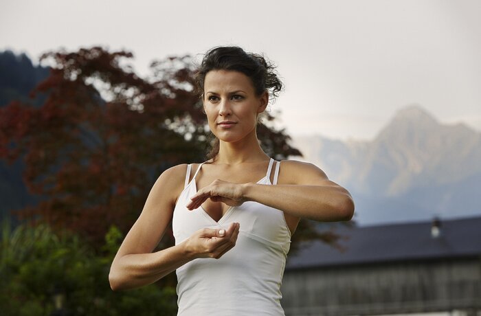 Frau in weißem Top praktiziert Yoga im Freien vor verschwommenem Hintergrund