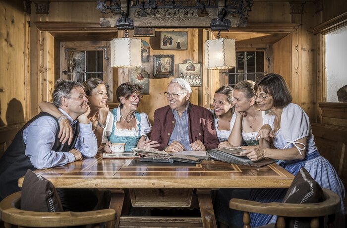 Familie Egger sitzt am Holztisch, umgeben von Holzvertäfelung und alten Bildern