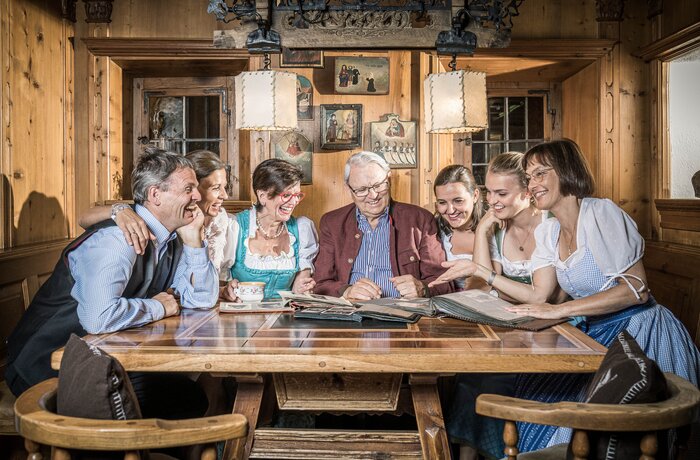 Familie Egger sitzt lachend um einen Holztisch und betrachtet ein Fotoalbum