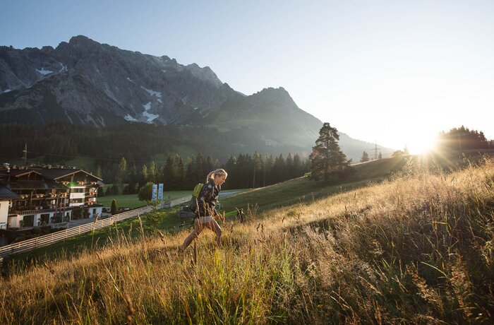 Woman walking through tall grass against a mountain backdrop