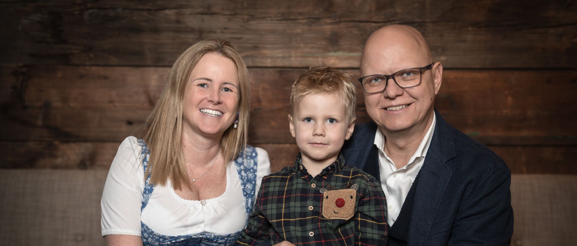 Family smiles at the camera in front of a wooden wall
